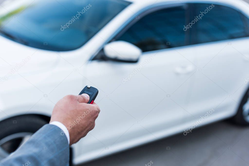 partial view of businessman with car keys in hand and car on background