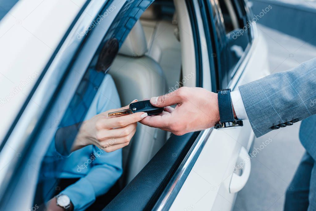 cropped shot of businessman giving car keys to colleague at driver seat in car