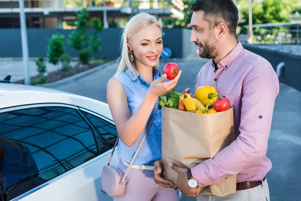 駐車場の車の近くに健康食品の紙袋と笑顔の結婚されていたカップルの肖像画 — ストック写真