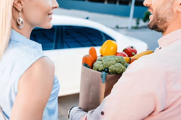 駐車場の車の近くに健康食品の完全な紙袋の結婚されていたカップルのクロップ撮影  — 無料ストックフォト