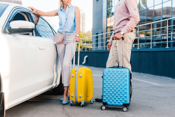 partial view of husband and wife with baggage standing at car on parking
