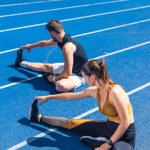 Высокий угол зрения молодых спортсменов мужского и женского бега, сидящих на беговой дорожке и растяжения