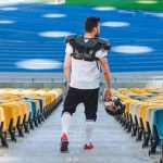 Vista trasera del joven jugador de fútbol americano en las escaleras en el estadio deportivo