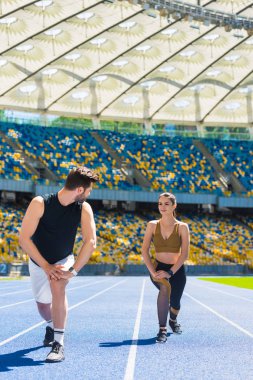 young athletic couple warming up legs before jogging on running track at sports stadium clipart