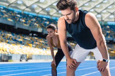 young tired couple standing on running track at sports stadium after jogging clipart