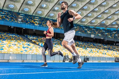 motion shot of young male and female joggers running on track at sports stadium clipart
