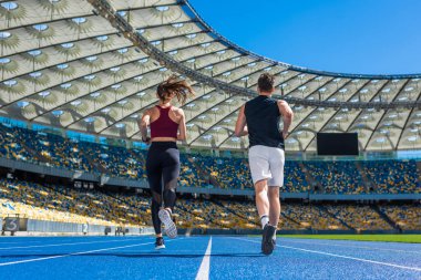 rear view of male and female joggers running on track at sports stadium clipart