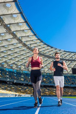 fit young male and female joggers running on track at sports stadium clipart