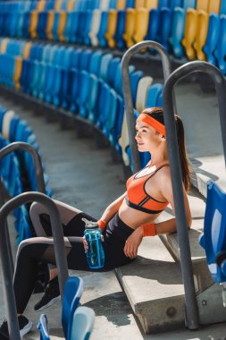 spor stadyumunda merdivenlerde oturan su olan yorgun kadın yan görünüm