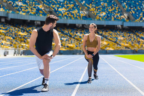 young fit couple warming up legs before jogging on running track at sports stadium