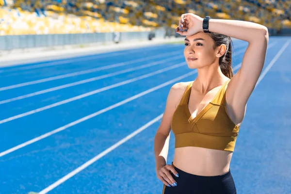 athletic female jogger wiping sweat after run on track at sports stadium