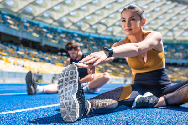 young active couple sitting on running track and stretching at sports stadium