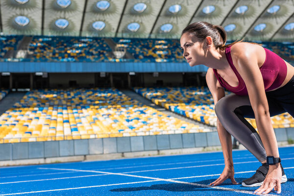 athletic female runner in start position on running track at sports stadium