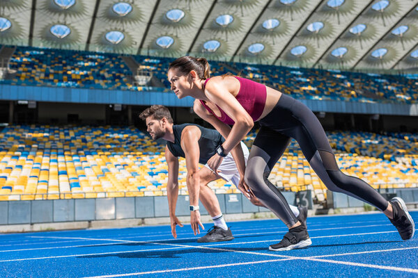 спортивные юноши и девушки-спринтеры в стартовой позиции на беговой дорожке на спортивном стадионе
