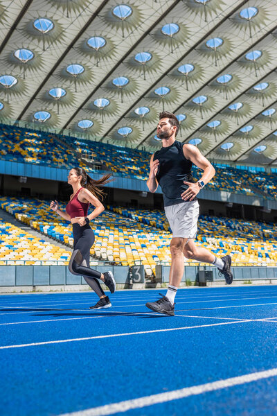 athletic young male and female joggers running on track at sports stadium