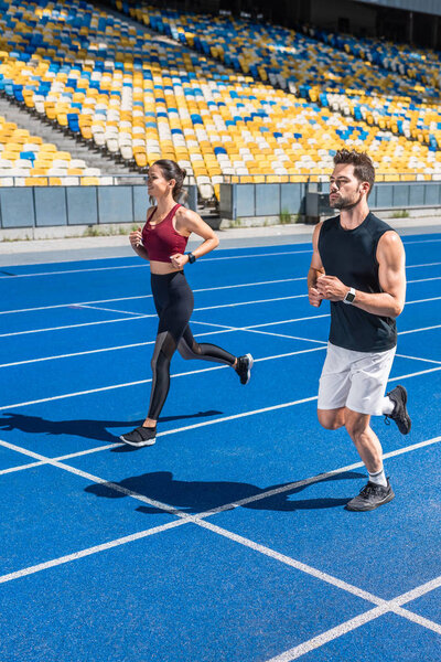 attractive young male and female joggers running on track at sports stadium
