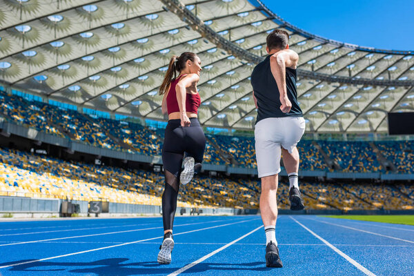 rear view of young male and female joggers running on track at sports stadium