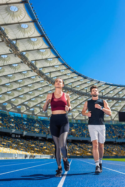 fit young male and female joggers running on track at sports stadium