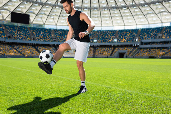 athletic young soccer player bouncing ball on leg at sports stadium
