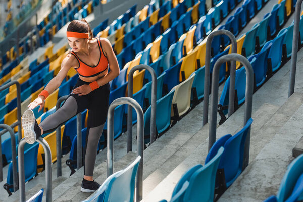 high angle view of beautiful young woman stretching on tribunes at sports stadium