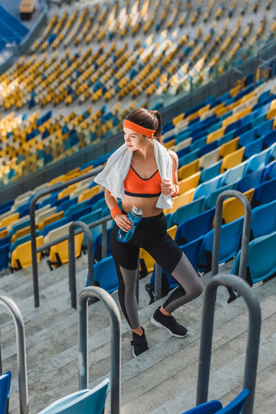 high angle view of attractive young woman with water bottle and towel at sports stadium