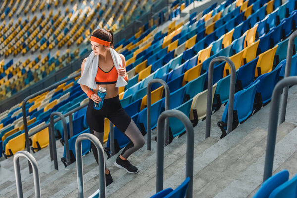 high angle view of beautiful young woman with water bottle and towel at sports stadium