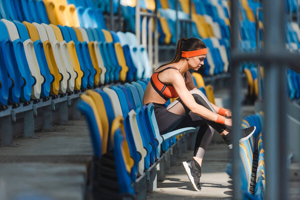 side view of sportive young woman sitting on tribunes at sports stadium