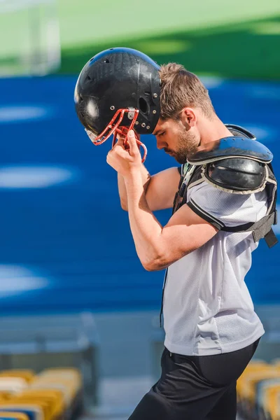 Genç Amerikan futbolu oyuncusu kask spor stadyumunda koyarak yan görünüm
