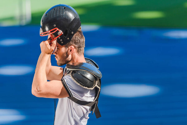 young american football player putting on helmet at sports stadium