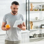 Vuxen man med digitala tablett holding orange och letar efter recept på kök