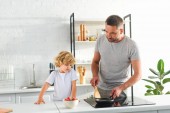 Mann heizt Pfanne an, während sein Sohn in der Nähe der Küche steht 