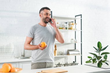 gülümseyen, önden görünüm dostum smartphone üzerinde konuşmak ve turuncu mutfak üzerinde tutan