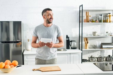 gülümseyen adam tablo yakınındaki dijital tablet mutfak üzerinde tutan 