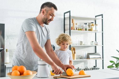 adam kesme turuncu bıçak, oğlu yakınındaki mutfak ayakta iken taze meyve suyu yapmak için