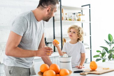 son and father looking at each other after making fresh orange juice at kithen clipart