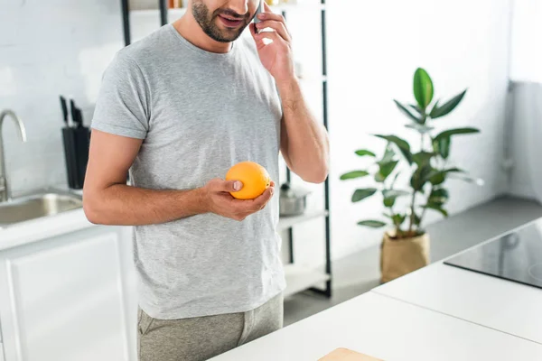 Обрезанный Образ Человека Разговаривающего Смартфоне Держащего Апельсин Кухне — Бесплатное стоковое фото