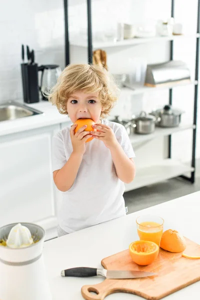 Menino Comendo Laranja Perto Mesa Com Placa Corte Faca Cozinha — Fotografia de Stock