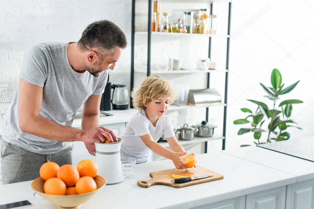 happy family making fresh orange juice by squeezer on table at kitchen 