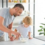 成年男子把牛奶倒入碗, 而他的儿子站在厨房附近