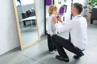 rear view of father helping son tying necktie at home  clipart