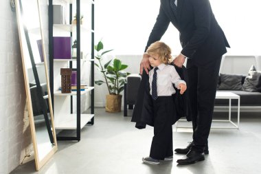 cropped image of man in suit helping son to putting on jacket at home  clipart