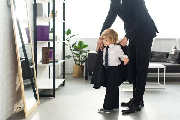 cropped image of man in suit helping son to putting on jacket at home 