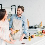 Boyfriend pouring wine into glass and looking at girlfriend in kitchen