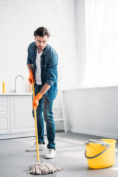 handsome man cleaning floor in kitchen with mop