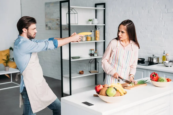 Girlfriend Cutting Vegetables Serious Boyfriend Having Fun Banana Gun Kitchen — Stock Photo, Image