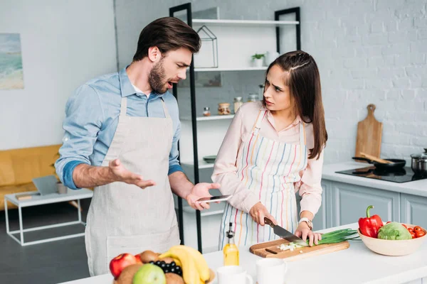 Irritado Namorado Gesticulando Enquanto Namorada Cortando Legumes Cozinha — Fotografia de Stock