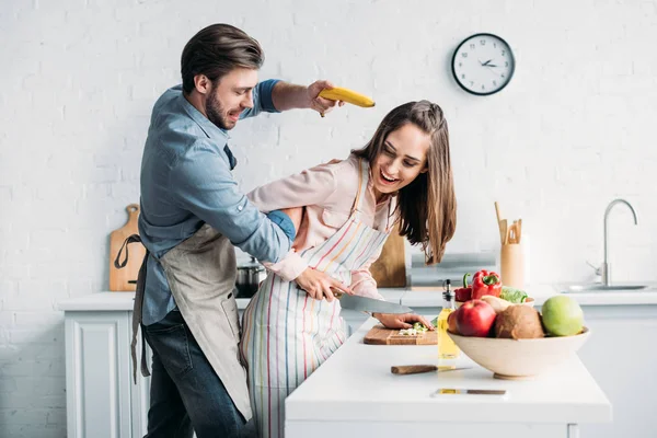 Girlfriend Cutting Vegetables Boyfriend Having Fun Banana Gun Kitchen — Free Stock Photo