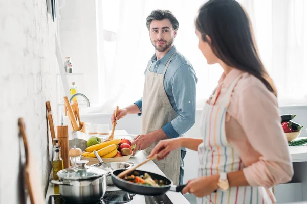 キッチンで彼氏を見てフライパンで野菜をフライパンのガール フレンド — ストック写真