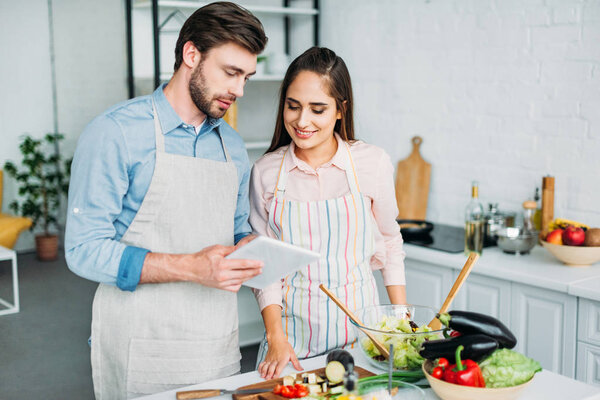 couple looking at tablet with recipe while cooking in kitchen