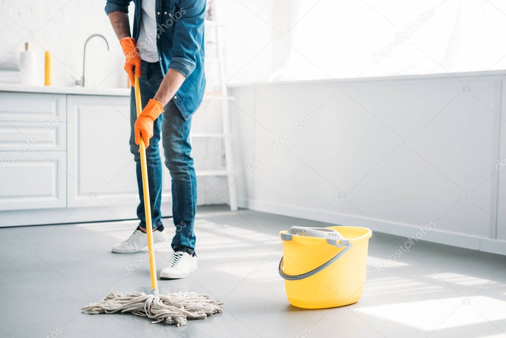 cropped image of man cleaning floor in kitchen with mop